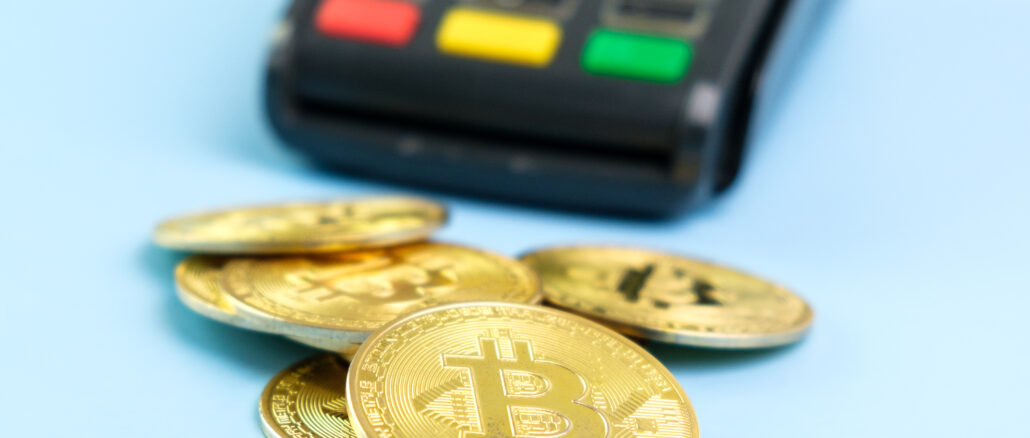 Bitcoin coins near POS payment terminal on the blue background. Crypto currency for payment